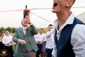 Groom playing the bouquet ribbon game with a bottle of whisky in Oberhausbergen, France during a wedding reception party.